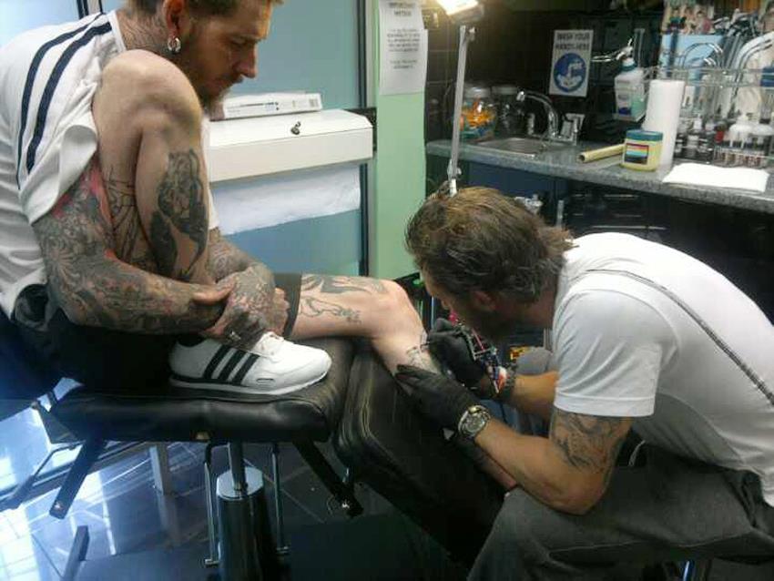 Tom tattooing his signature on his tattooist