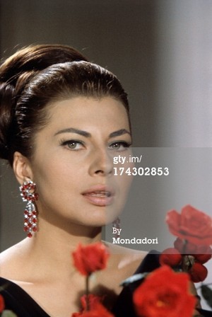 next to a bunch of long stem red roses in her villa in the Appia Antica. Rome (Italy), 1964