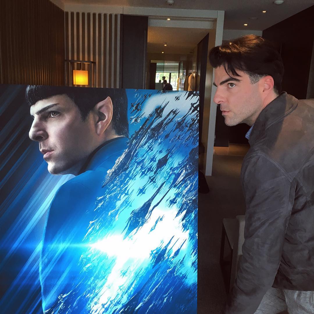 Zachary Quinto posing next to a poster of Spock